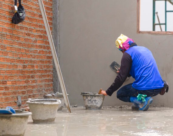 Rear side view of Asian builder using trowel to polishing concrete wall in house construction site